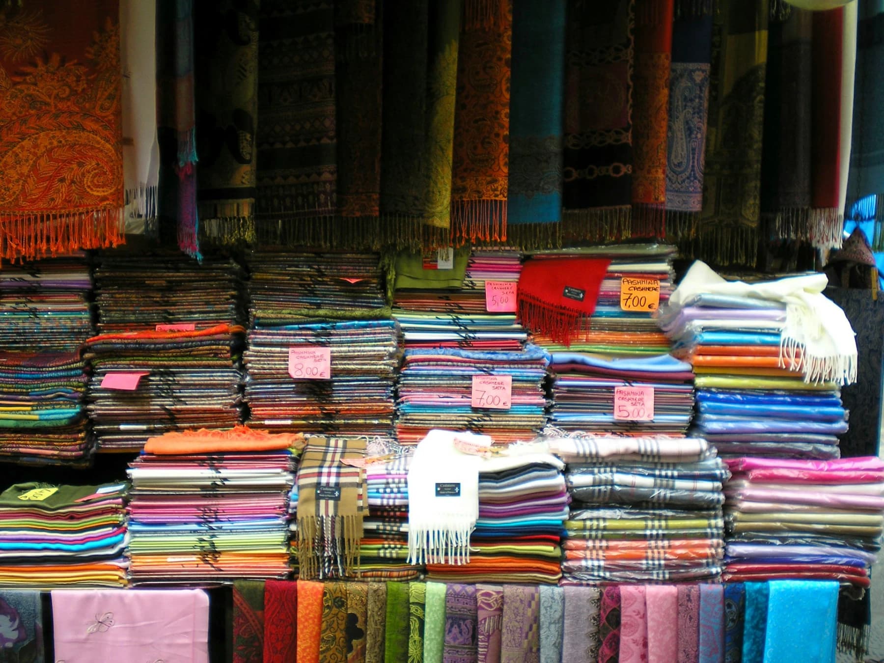 Market stall stacked with folded pashmina and cashmere scarves in Rome
